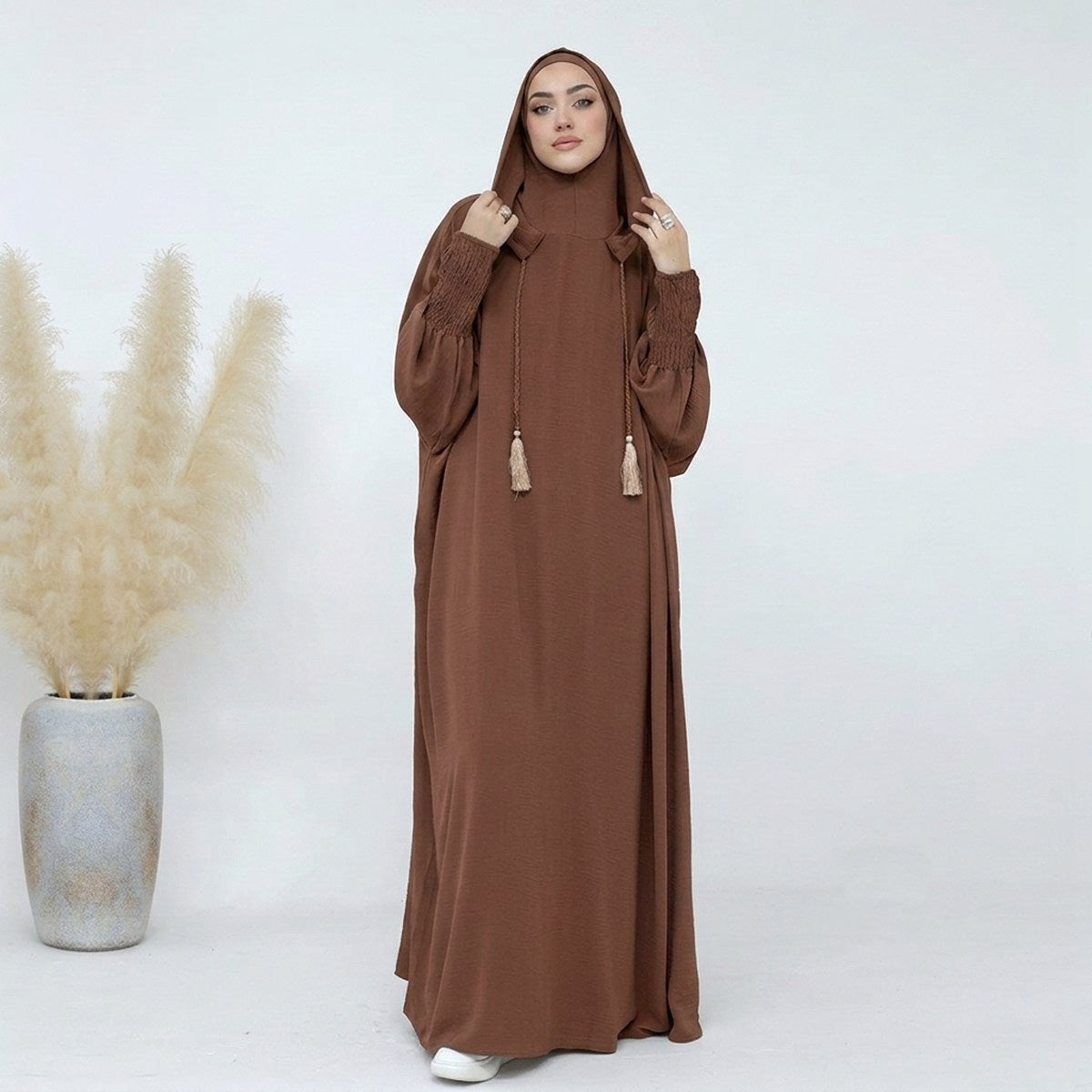 Coffee hooded abaya jilbab, front view, flowing silhouette with smocked cuffs and tassel ties