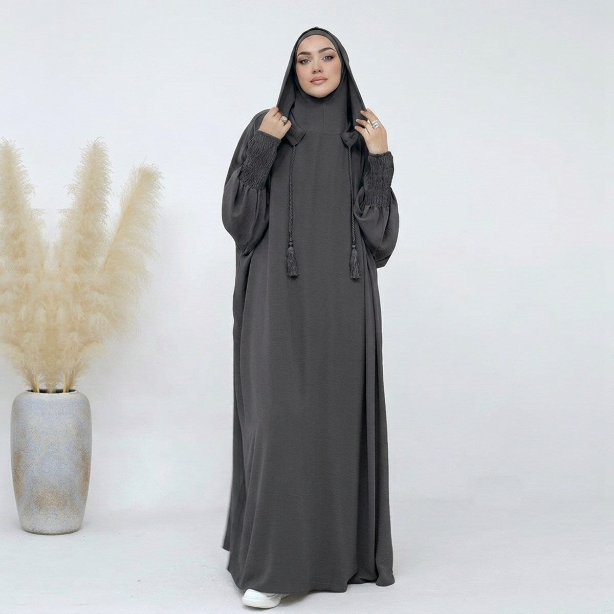 Dark grey hooded jilbab abaya, full-length front view, relaxed smocked sleeves and tassels